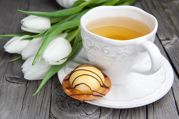 Pastel dulce con taza de té y flores sobre mesa de madera — Foto de Stock