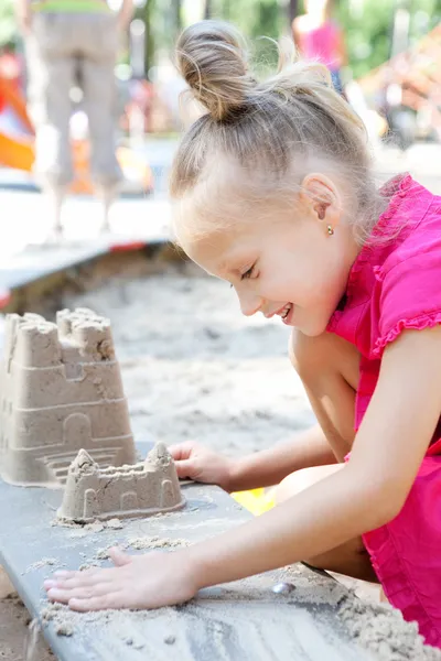 Piccola ragazza felice costruendo un castello di sabbia nella sabbiera — Foto Stock