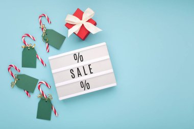 Beyaz ışıklı kutuda kırmızı hediye kutusu ve mavi kağıtta Noel şeker kamışları var. Kış sonu satışının tanıtımı için tasarım. Üst görünüm, boşluğu kopyala. Yeşil Pazartesi Satışı konsepti.