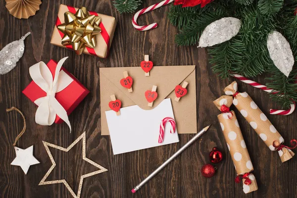 空の白い休日カード 赤い花のポインセチア クリスマスの装飾 ギフトボックスや暗い木製の背景にキャンディーの缶 フラットレイアウト トップビュー コピースペース お祝いの手作りギフトコンセプト — ストック写真