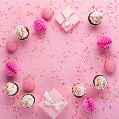 Doğum günü, kadın ya da anneler günü için bayram tebrik kartı. Pembe kağıt süslemeler, tatlı kurabiyeler ve pembe serpiştirilmiş kekler. Düz yatış, üst görünüm.