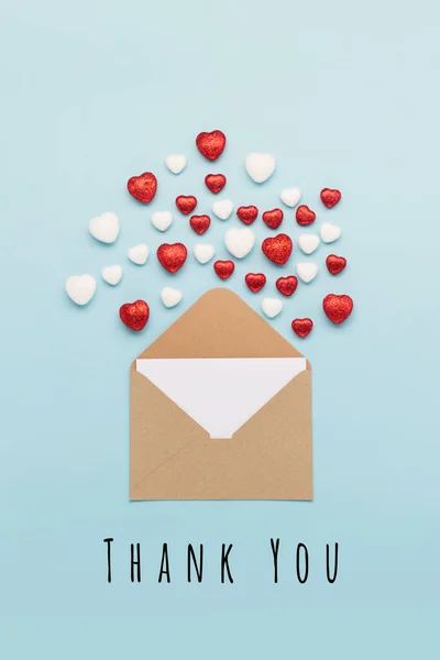 International Thank You Day, Thankfulness concept. Thank You or thanks greeting card with empty envelope and red hearts on pastel blue background, top view, flat lay, copy space.