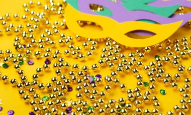 Maskeli karnaval maskeli Mardi Gras altın renkli boncuklar ve sarı arka planda altın, yeşil, mor konfeti. Parti davetiyesi, tebrik kartı, Venedik karnavalı kutlama konsepti..