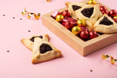 Purim bayramı Yahudi karnavalı konsepti. Lezzetli hamantaschen kurabiyeleri, kırmızı karnaval maskesi, gürültü çıkarıcı, tatlı şekerler ve pembe arka planda parti dekoru. Üst görünüm, düz görünüm, kopyalama alanı.