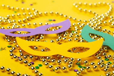 Mardi Gras Maskeli Balo Festivali maskeleri, altın rengi boncuklar ve sarı arka planda altın, yeşil, mor konfeti. Parti davetiyesi, tebrik kartı, Venedik karnaval kutlaması konsepti
