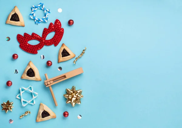 普林庆祝犹太人狂欢节的概念 味道鲜美的哈曼曲奇 红色狂欢节面具 吵闹者 甜糖果和蓝色背景的派对装饰 顶视图 复制空间 — 图库照片