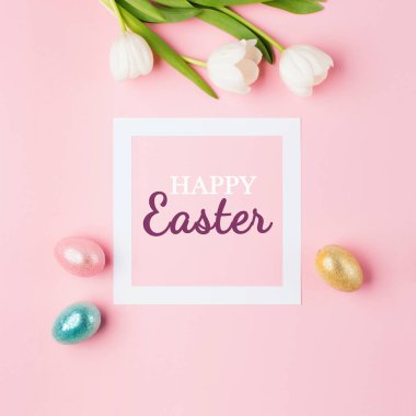 Altın, pembe arka planda parlak Paskalya yumurtaları, yazılı beyaz çerçeve Mutlu Paskalyalar, lale çiçekleri buketi. Düz yerde, üst tarafta. Paskalya dekorasyonu, folyo minimalist yumurta tasarımı, modern tatil kartı konsepti..