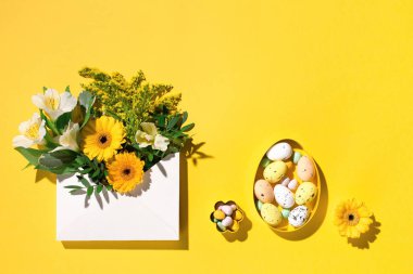 Bayramlık Paskalya çiçeği kompozisyonu. Sarı ve beyaz çiçekler, kağıt sarısı arkaplanda pastel paskalya yumurtaları. Bahar, Paskalya kartı konsepti. Düz konum, üst görünüm, kopyalama alanı.