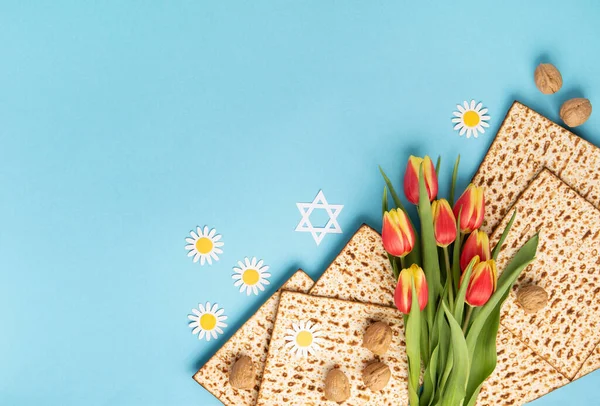 Yahudi bayramı tebrik kartı konsepti. Matza, fındık, lale ve papatya çiçekli mavi masa. Seder Pesach bahar tatili arka planı, üst görünüm, kopyalama alanı.