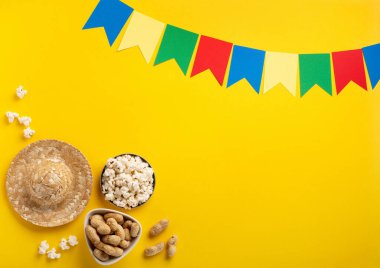 Brezilya Karnavalı Festa Junina Yaz Festivali konsepti. Brezilya hasır şapkası, patlamış mısır, fıstık ve sarı arka planda renkli bayraklar, üst manzara. Tebrik Kartı, Davetiye veya Tatil Posteri Tasarımı