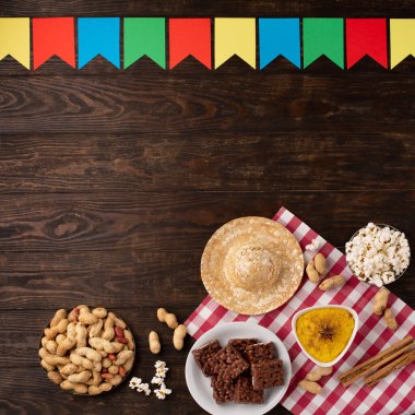Junina Yaz Festivali Karnavalı konsepti. Brezilya hasır şapkası, patlamış mısır, fıstık ve ahşap arka planda renkli bayraklar, üst manzara. Tebrik Kartı, Davetiye veya Tatil Posteri Tasarımı