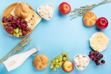 Mutlu Shavuot bayram kartları, Yahudi dini bayramı konsepti. Süt ürünleri, meyveler, peynir, ekmek, mavi arka planda süt şişesi. Düz konum, üst görünüm, kopyalama alanı.