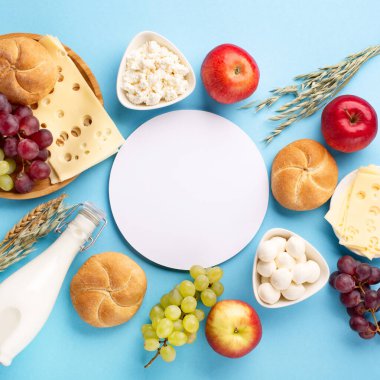 Mutlu Shavuot bayram kartları, Yahudi dini bayramı konsepti. Süt ürünleri, meyveler, peynir, ekmek, mavi arka planda süt şişesi. Düz konum, üst görünüm, kopyalama alanı.