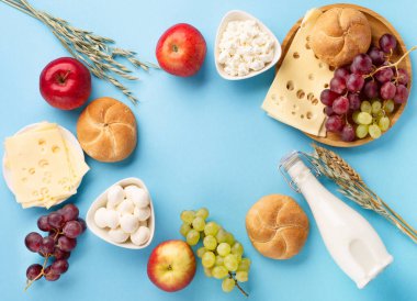 Mutlu Shavuot bayram kartları, Yahudi dini bayramı konsepti. Süt ürünleri, meyveler, peynir, ekmek, mavi arka planda süt şişesi. Düz konum, üst görünüm, kopyalama alanı.