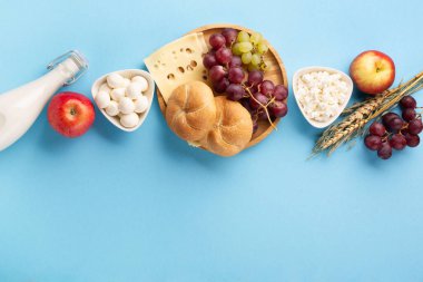 Mutlu Shavuot bayram kartları, Yahudi dini bayramı konsepti. Süt ürünleri, meyveler, peynir, ekmek, mavi arka planda süt şişesi. Düz konum, üst görünüm, kopyalama alanı.