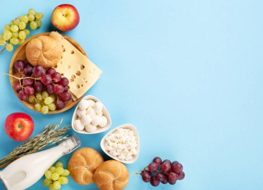 Mutlu Shavuot bayram kartları, Yahudi dini bayramı konsepti. Süt ürünleri, meyveler, peynir, ekmek, mavi arka planda süt şişesi. Düz konum, üst görünüm, kopyalama alanı.