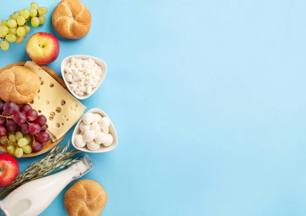Mutlu Shavuot bayram kartları, Yahudi dini bayramı konsepti. Süt ürünleri, meyveler, peynir, ekmek, mavi arka planda süt şişesi. Düz konum, üst görünüm, kopyalama alanı.