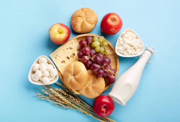 Mutlu Shavuot bayram kartları, Yahudi dini bayramı konsepti. Süt ürünleri, meyveler, peynir, ekmek, mavi arka planda süt şişesi. Düz konum, üst görünüm, kopyalama alanı.