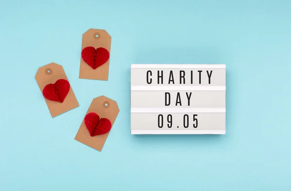 International Day of Charity, September 5. Charity, give help, donations, support, humanitarian aid day concept with text on white lightbox, red paper hearts  on blue background.