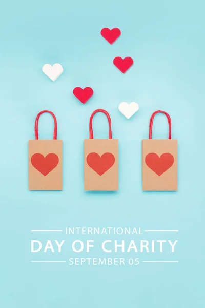 International Day of Charity, 5 September. Charity, give help, donations support concept with text message, red  hearts and paper bags on blue background.