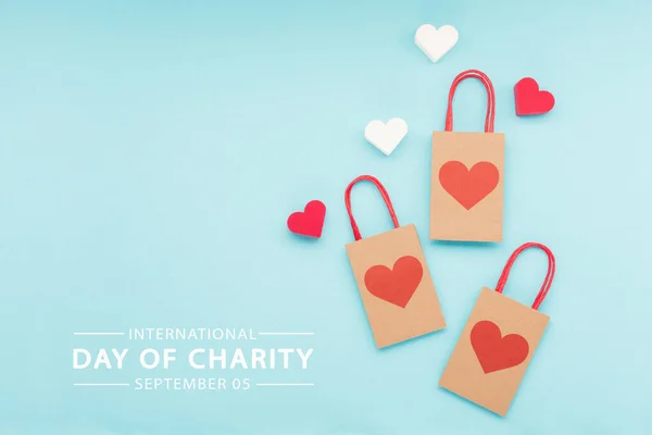 International Day of Charity, 5 September. Charity, give help, donations support concept with text message, red  hearts and paper bags on blue background.