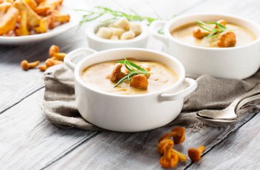 Homemade Mushroom cream soup with chanterelles and herbs on white rustic wooden background, selective focus. Autumn handmade food concept.