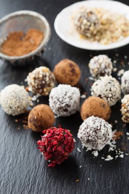 Ev yapımı şeker, şekersiz çikolata ve fındık şekerli, kakao tozu, hindistan cevizi, böğürtlen ve kesilmiş fındıklı siyah taş arka plan, seçici odaklanma. Sağlıklı yeme kavramı.