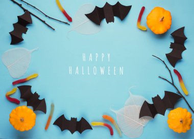 Cadılar bayramı konseptin kutlu olsun. Cadılar Bayramı süslemeleri, yarasalar, balkabakları, şeker ve ağaç dalları mavi arka planda. Fotokopi alanı olan Cadılar Bayramı partisi tebrik kartı modeli. Düz yerde, üst tarafta, tepede. Asgari biçim