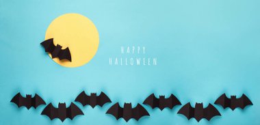 Mavi arka planda Cadılar Bayramı kağıt süslemeleri. Kara yarasalar ve ay. Cadılar Bayramı konsepti Düz yerde, üst tarafta, tepede. Asgari düzeyde. Fotokopi alanı olan Cadılar Bayramı partisi tebrik kartı maketi. 