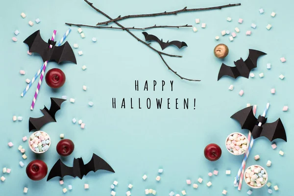 Happy Halloween holiday concept. Halloween decorations, paper black bats, candy on blue background. Halloween party greeting card mockup, copy space. Flat lay, top view, overhead.