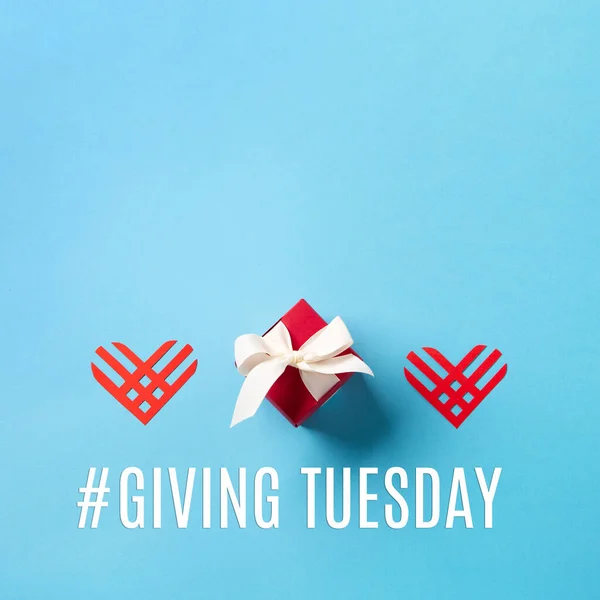 Giving Tuesday, global day of charitable giving after Black Friday shopping day. Charity, give help, donations support concept. Red paper hearts and gift box on blue background. Top view, copy space.