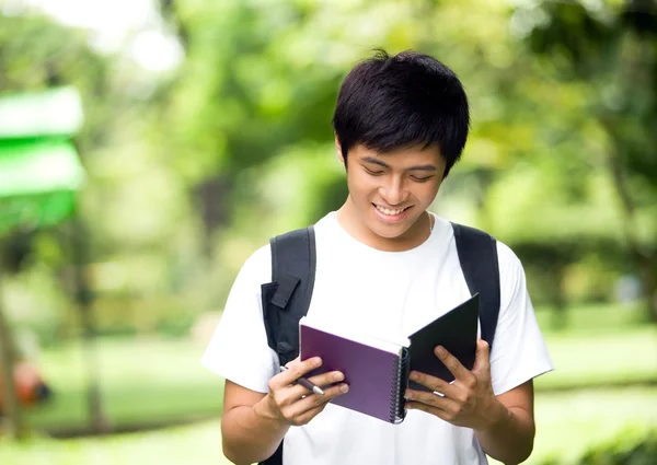 Asian young handsome guy open a book and smile in the park — Stock Photo, Image