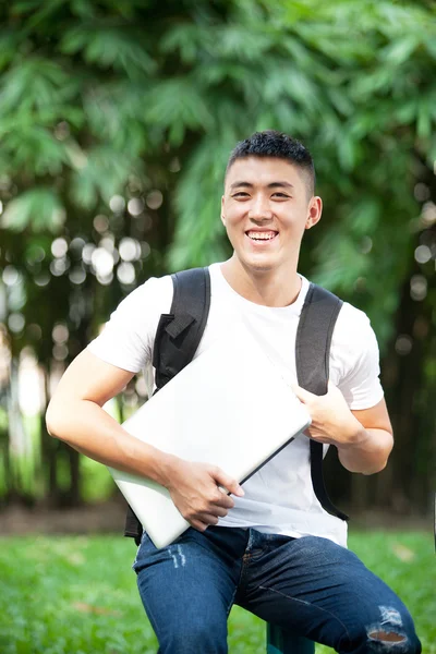 Giovane bello studente asiatico con computer portatile nel parco — Foto Stock