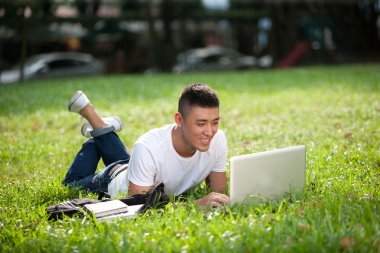 genç yakışıklı Asya öğrenci dizüstü bilgisayar ve kapıdan dışarı kulaklık