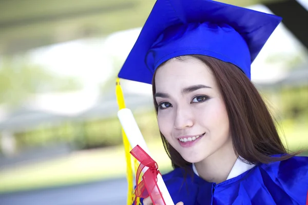 Portrait of a beautiful young asian woman in graduation cap and gown standing outside on campus — Stock Photo, Image