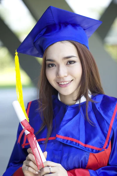 Portret van een mooie jonge Aziatische vrouw in afstuderen cap en jurk staande buiten op de campus — Stockfoto