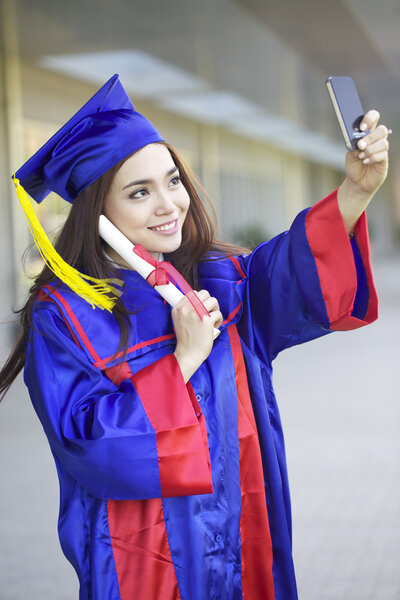 portrait of a beautiful young asian woman in graduation cap and gown standing outside on campus