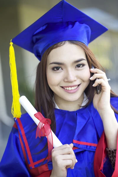 Portrait of a beautiful young asian woman in graduation cap and gown standing outside on campus — Stock Photo, Image