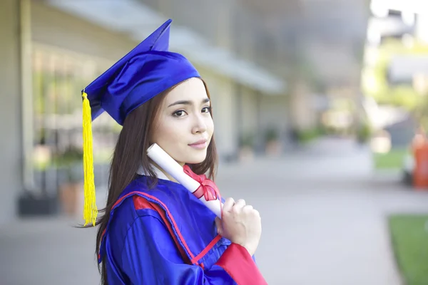 Portrait of a beautiful young asian woman in graduation cap and gown standing outside on campus — Stock Photo, Image