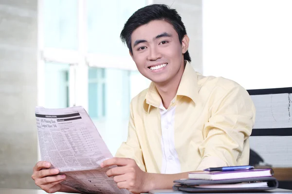 Щасливий азіатський молодий бізнесмен читає газету і посміхається — стокове фото