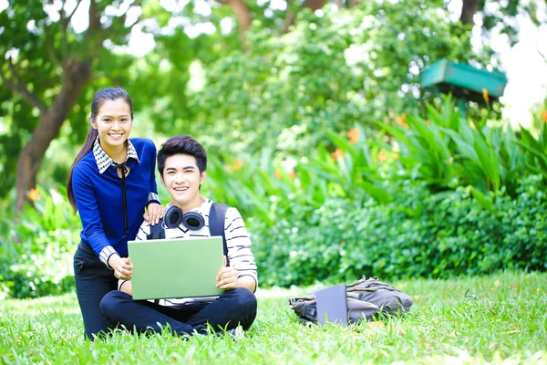Jóvenes estudiantes asiáticos con computadora y sonrisa al aire libre —  Fotos de Stock