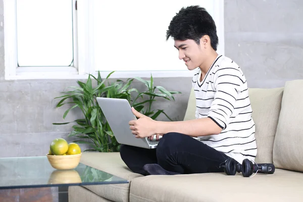Młody chiński człowiek za pomocą laptopa, relaksując się na kanapie w domu — Zdjęcie stockowe