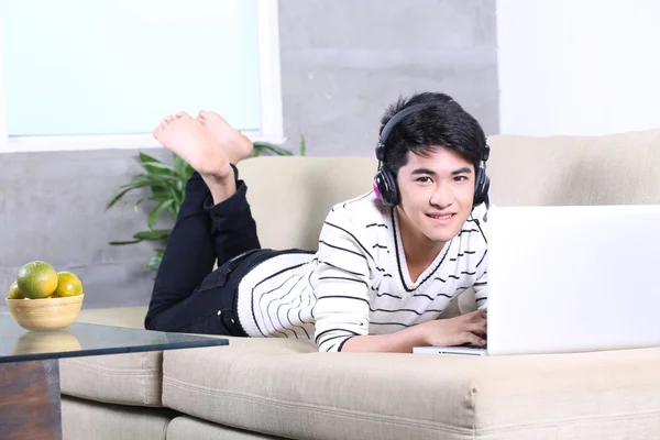 Asiatiska ung man liggande på tränare i vardagsrum och surfa internet, läsa böcker — Stockfoto