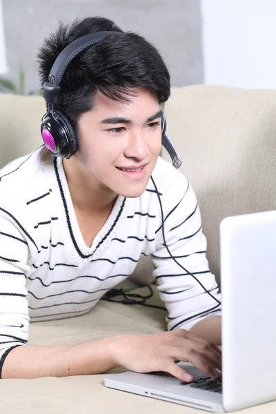 Asian young man lying on the coach in living room and surfing internet, reading books — Stock Photo, Image