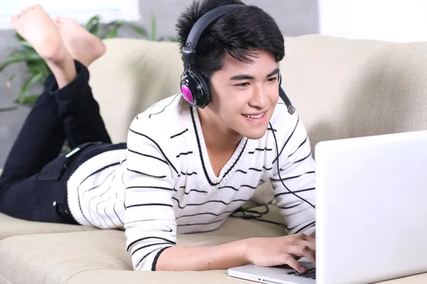 Asian young man lying on the coach in living room and surfing internet, reading books — Stock Photo, Image