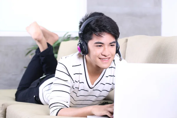 Asian young man lying on the coach in living room and surfing internet, reading books — Stock Photo, Image