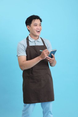 Garson üniformalı Asyalı yakışıklı adam, hoş geldin misafir ve sipariş, mavi arka planda izole.