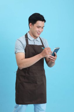 Garson üniformalı Asyalı yakışıklı adam, hoş geldin misafir ve sipariş, mavi arka planda izole.
