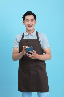 Garson üniformalı Asyalı yakışıklı adam, hoş geldin misafir ve sipariş, mavi arka planda izole.