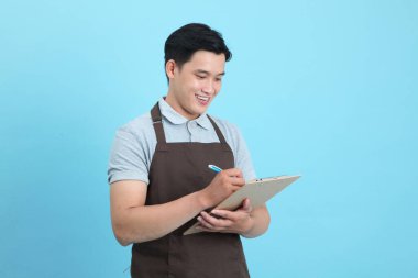 Garson üniformalı Asyalı yakışıklı adam, hoş geldin misafir ve sipariş, mavi arka planda izole.